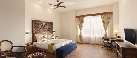 A hotel room with a bed, a desk, a chair, a television, and a ceiling fan.