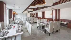 A modern dining area with multiple tables and chairs, a high ceiling with wooden slats, and pendant lighting. - Clarks Resort Birgunj (Birgunj)