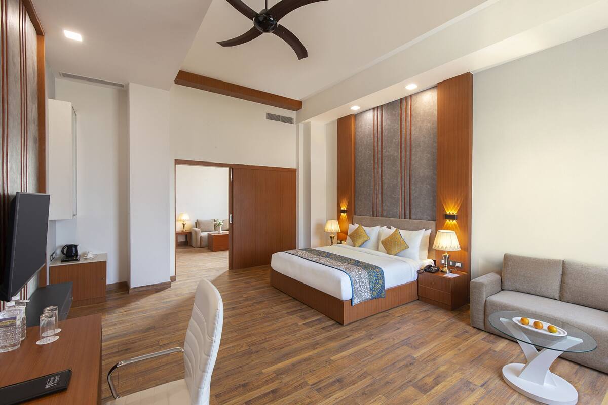 A hotel room with a bed, a desk, a chair, a sofa, a TV, and a ceiling fan.
