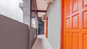 A corridor with a tiled floor, a grey wall, and a red door. - Hotel O Nakula Sadewa (Depok)