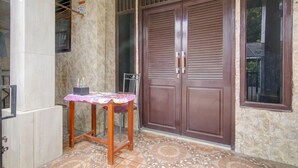 A room with a tiled floor, a wooden table with a pink tablecloth, a chair, and a large brown door with a window. - Hotel O Nakula Sadewa (Depok)