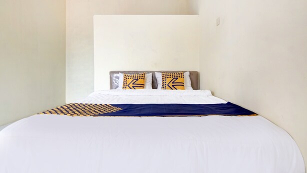 A neatly made bed with a white and blue bedspread, two pillows with geometric patterns, and a headboard against a plain wall. - Hotel O Nakula Sadewa (Depok)