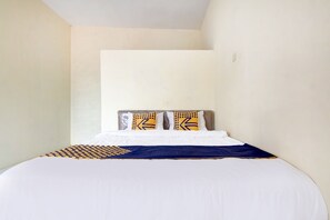 A neatly made bed with a white and blue bedspread, two pillows with geometric patterns, and a headboard against a plain wall. - Hotel O Nakula Sadewa (Depok)