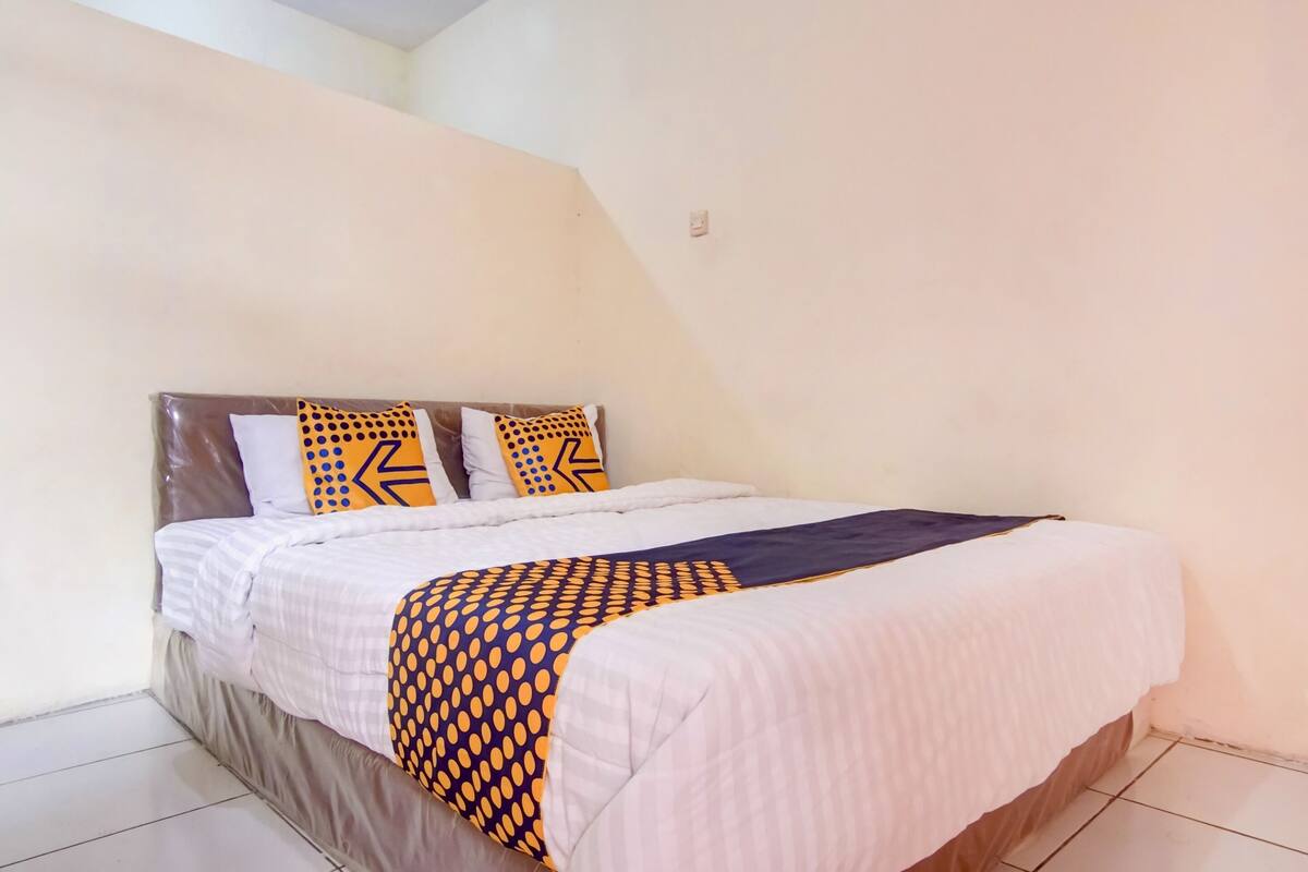 A neatly made bed with a patterned blanket and pillows, a dark headboard, and a plain wall.