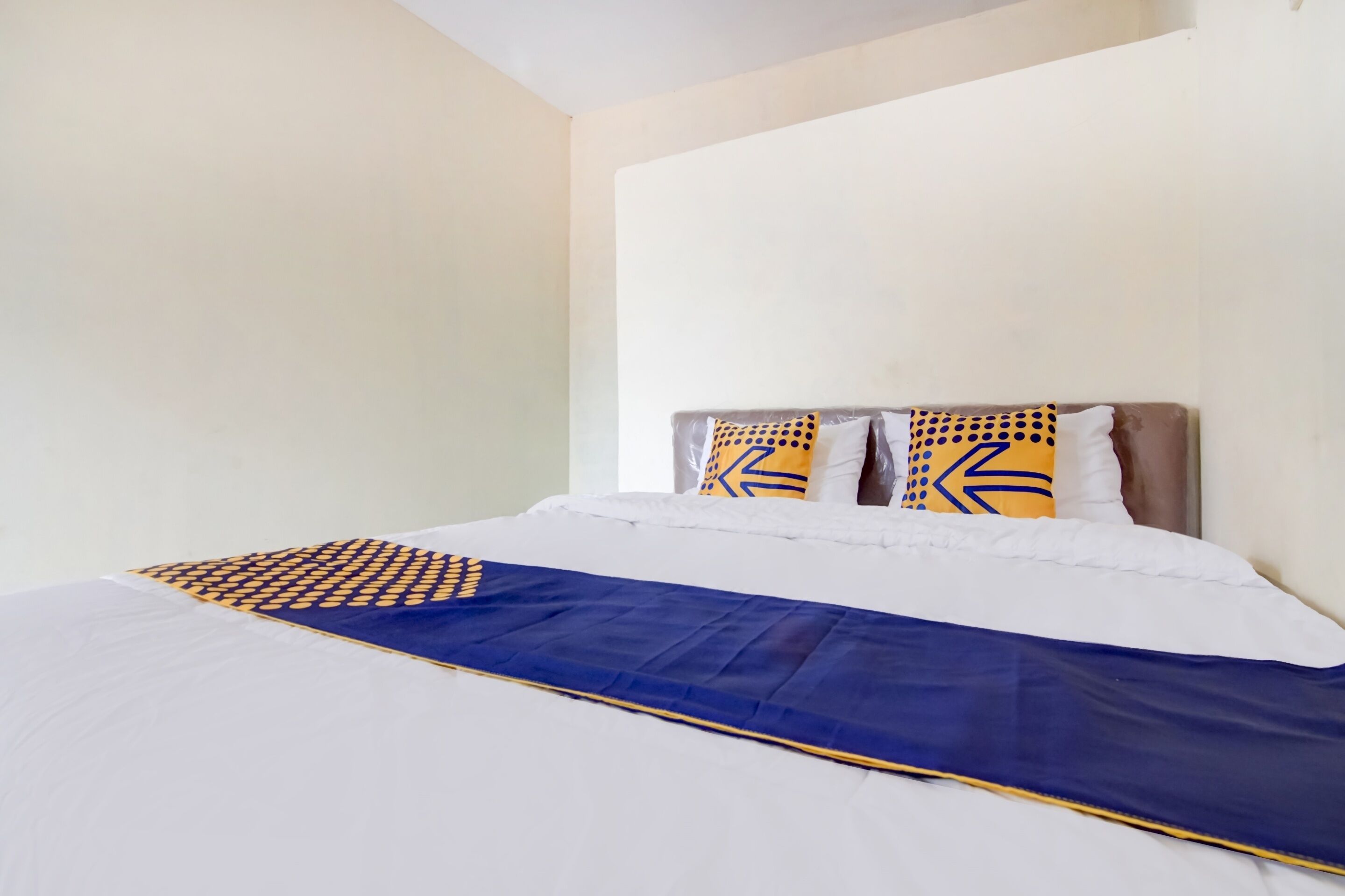 A neatly made bed with a blue and white bedspread, two pillows with geometric patterns, and a headboard against a plain wall.