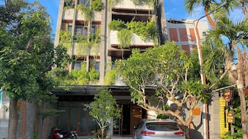 Un immeuble à plusieurs étages doté de balcons, une voiture garée et de la verdure environnante.