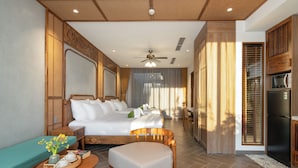 Quarto de hotel com cama, área de estar com mesa e cozinha compacta.