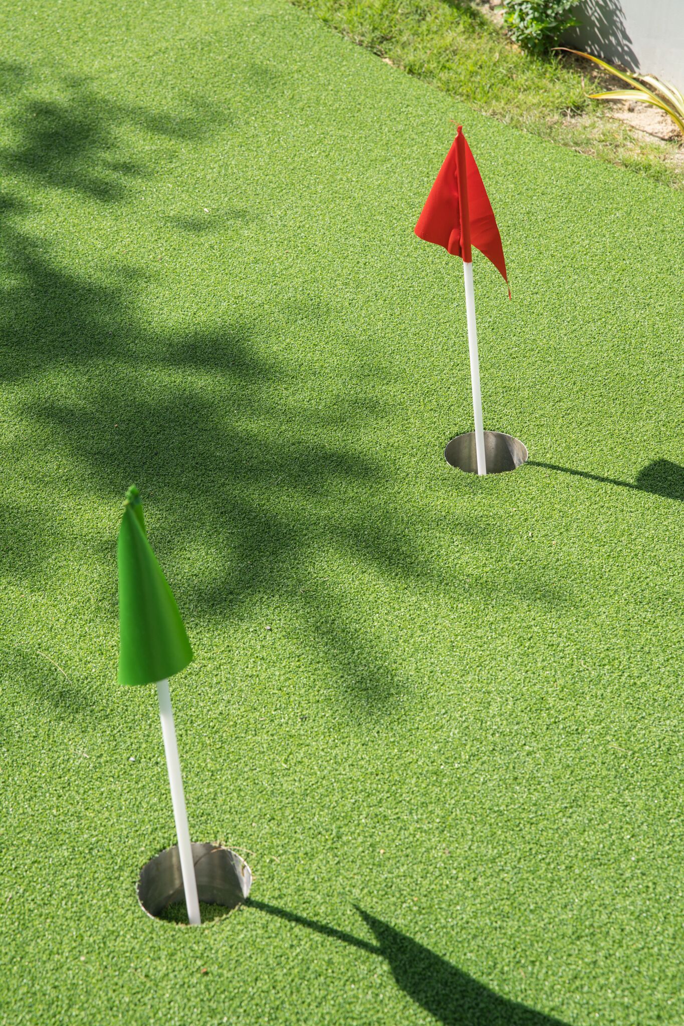Two golf flags on a green surface with shadows.