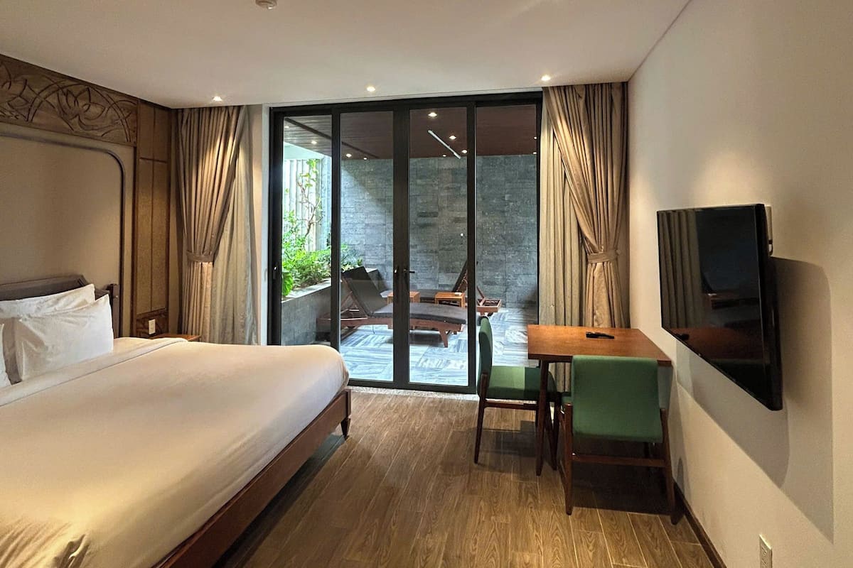 A hotel room with a bed, a desk, a TV, and a sliding glass door leading to an outdoor area.