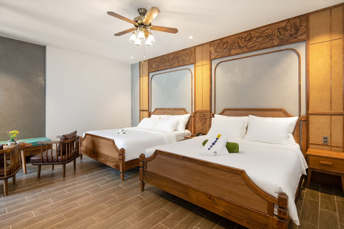 A hotel room with two wooden beds, a desk with a chair, and a ceiling fan.