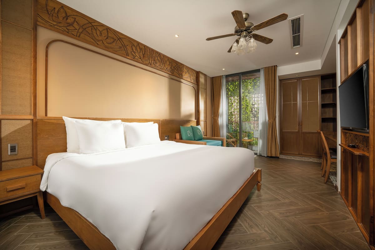 A spacious bedroom with a large bed, wooden headboard, a ceiling fan, and a TV.