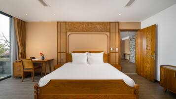 A modern hotel room with a large bed, wooden headboard, a desk with a chair, and a view through a large window.
