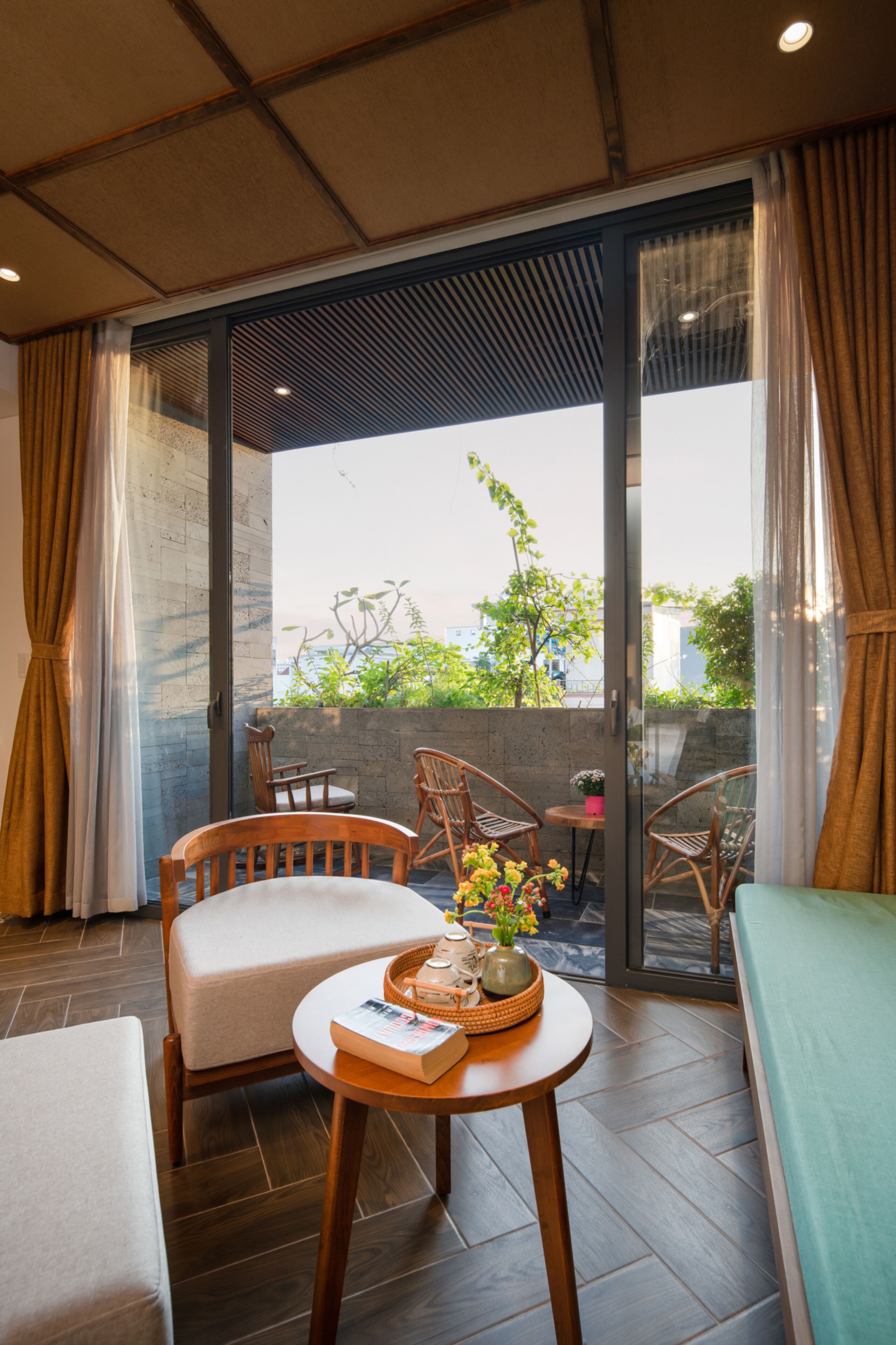 A balcony with wooden chairs, a small table with a vase of flowers, and a view of greenery and buildings.