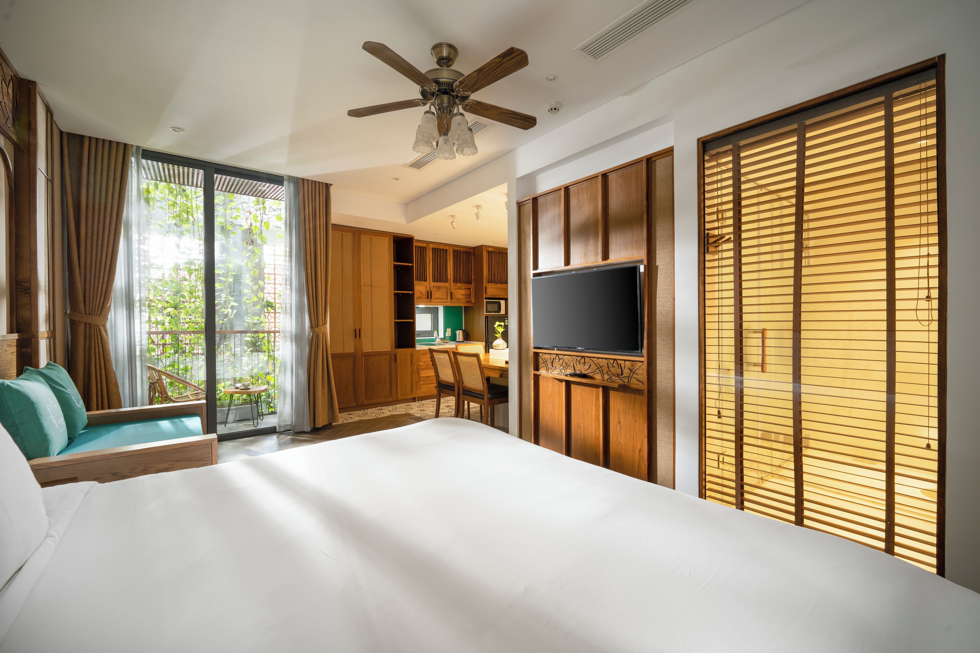 Ein Hotelzimmer mit Bett, Fernseher, Deckenventilator und einer Schiebetür zum Balkon.