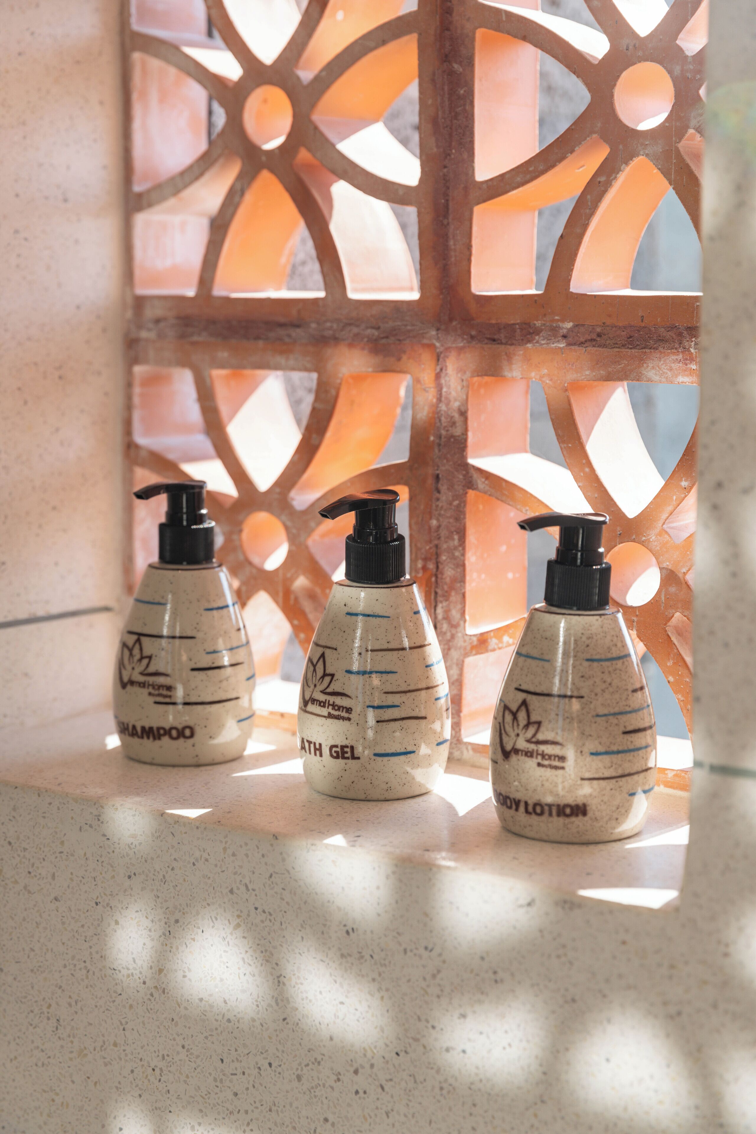 Three bottles of toiletries on a countertop with a decorative window in the background.