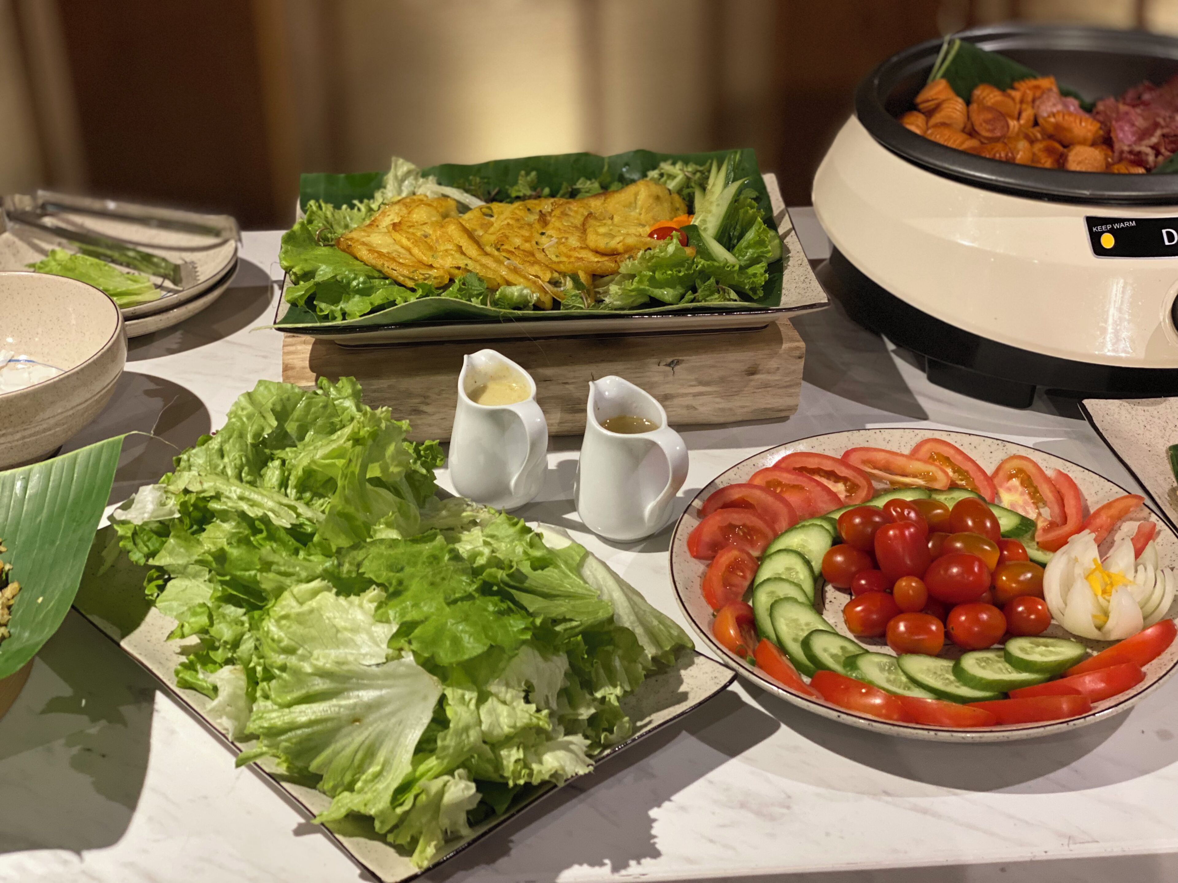 Una mesa de bufé con diversos platos, incluyendo una ensalada, un bol de vegetales cortados y una olla con comida caliente.