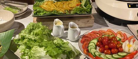 Una mesa de bufé con diversos platos, incluyendo una ensalada, un bol de vegetales cortados y una olla con comida caliente.