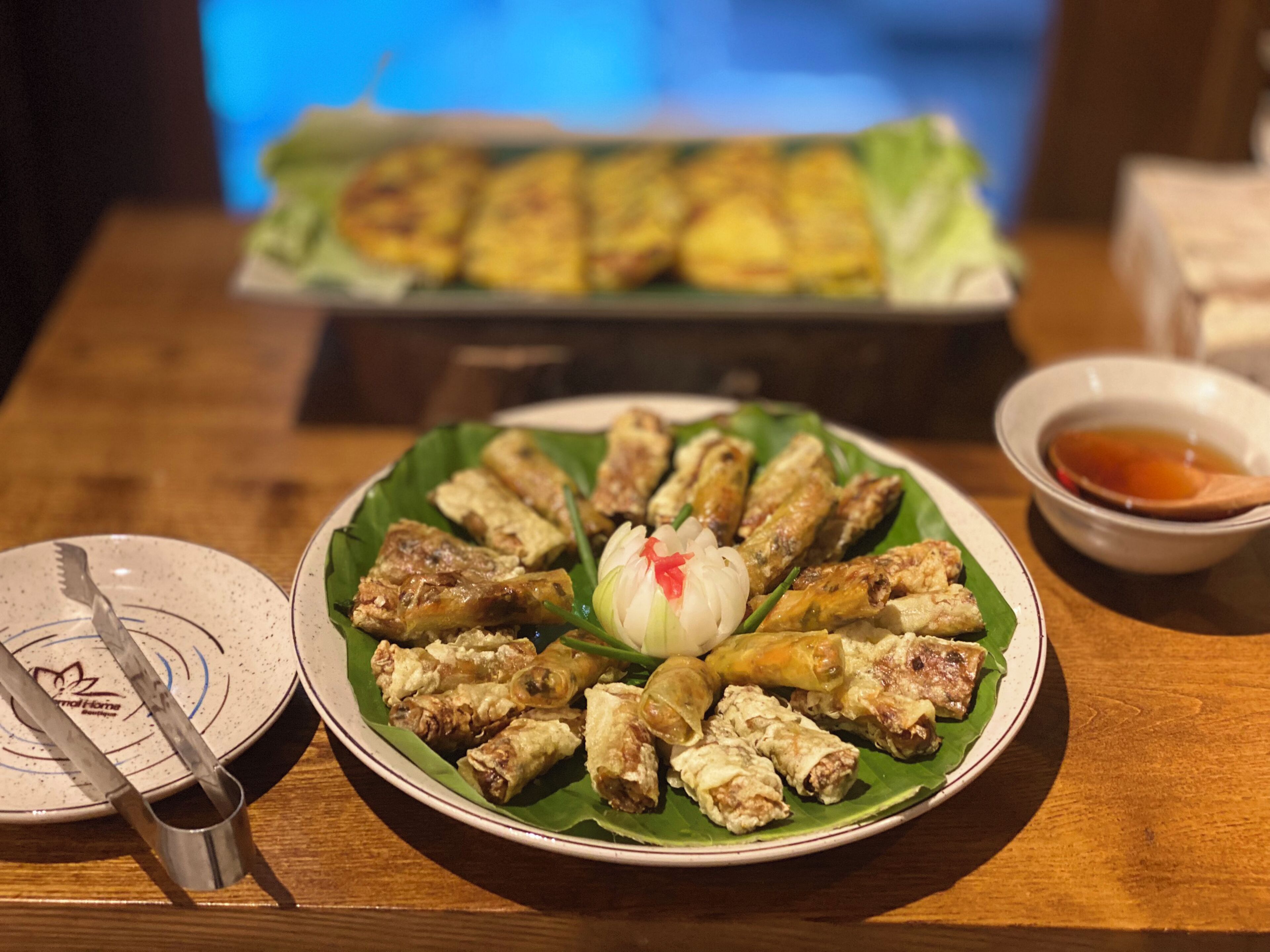 A plate of spring rolls on a wooden table with a bowl of sauce and a spoon.