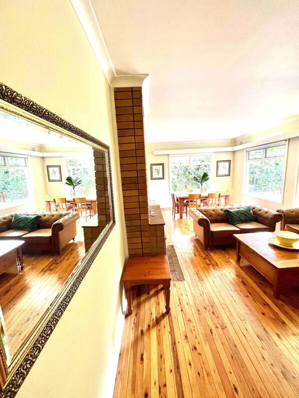 A spacious living room with a large mirror, wooden flooring, and multiple seating areas including sofas and a dining table. - Prime Spot! 5mins to “Grand Cliff Top Walk” & “3 Sisters” (Katoomba)