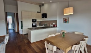 A modern kitchen with a central island, white cabinetry, a built-in oven, and a dining area with a wooden table and white chairs.