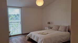 A bedroom with a bed, a nightstand, a lamp, and a window with blinds.