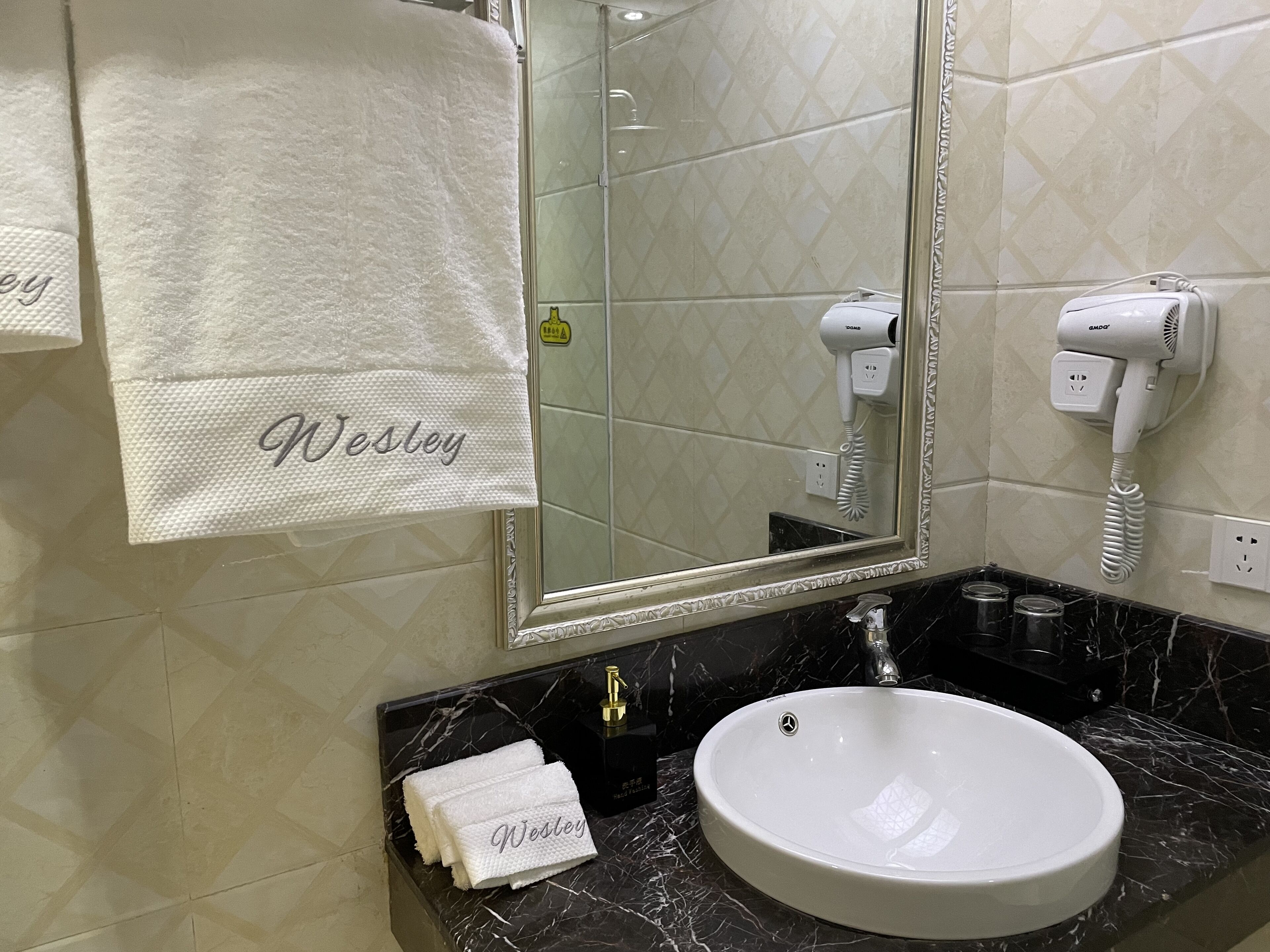 A bathroom with a white sink, a mirror, a hairdryer, and towels with the name 'Wesley' on them.
