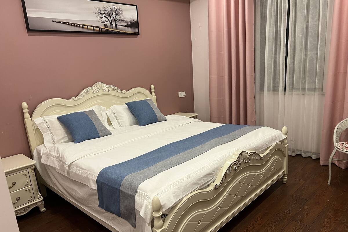 A neatly made bed with a white headboard, a nightstand with drawers, and a chair.