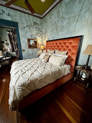 Une chambre Ă coucher avec un grand lit, une tĂȘte de lit, une table de chevet et un mur ornĂ© dâune fresque reprĂ©sentant un arbre dĂ©coratif.