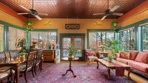 A spacious living room with a wooden ceiling, large windows, and a variety of furniture including a sofa, chairs, and a dining table.