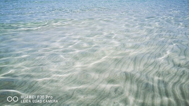 Una playa con aguas claras y poco profundas, y una costa distante.
