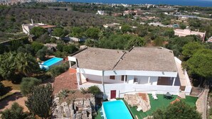 Una villa blanca con una gran piscina, rodeada de vegetación y vistas al mar.