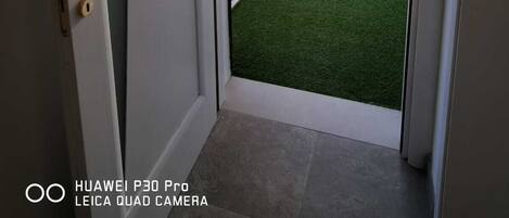 A door leading to a backyard with artificial grass and a bamboo fence.
