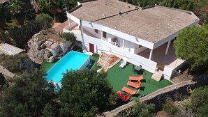 Una casa moderna de dos pisos con piscina, rodeada de vegetación y un paisaje montañoso.