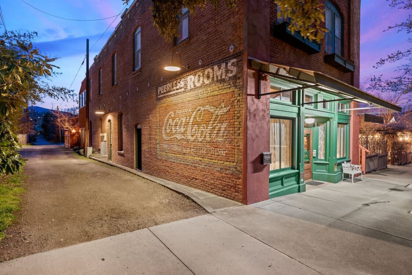 A brick building with a Coca-Cola mural, a green awning, and a sign for 'PEERLESS ROOMS'.