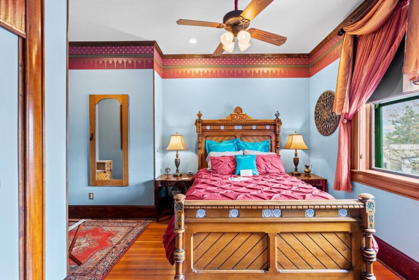 Ein traditionell eingerichtetes Schlafzimmer mit einem hölzernen Bett, zwei Nachttischlampen, einem Deckenventilator und einem großen Spiegel.