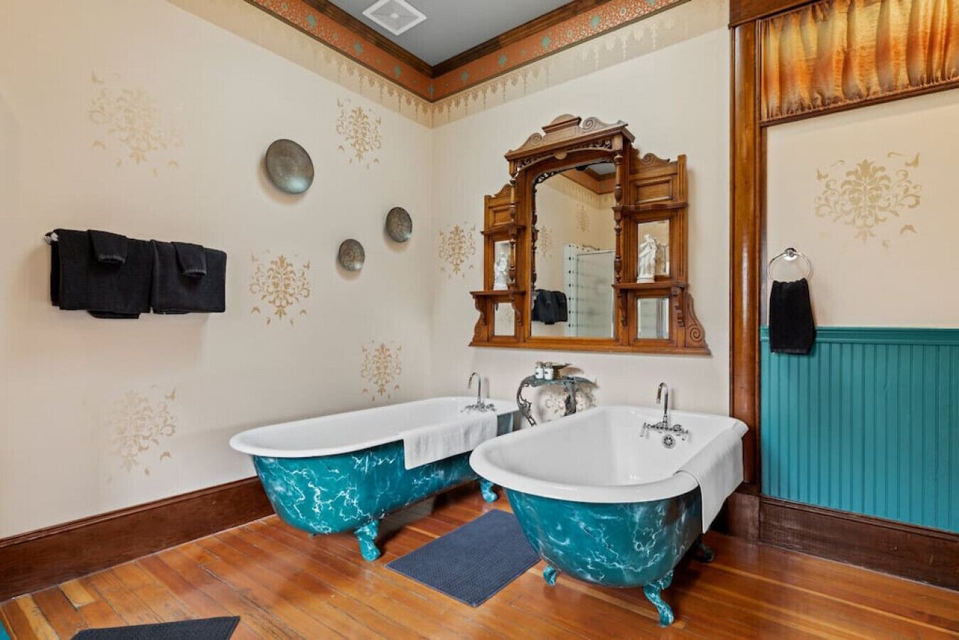 A bathroom with two clawfoot tubs, a large mirror, and decorative wall patterns.