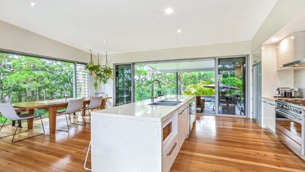 Una cocina moderna con una isla central, suelo de madera y ventanas amplias con vistas al exterior.