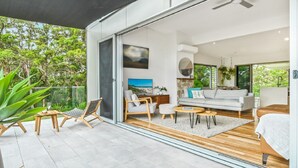 Una sala de estar moderna con un ventanal que da a un balcón, un conjunto de sofás, una mesa de centro y un televisor.