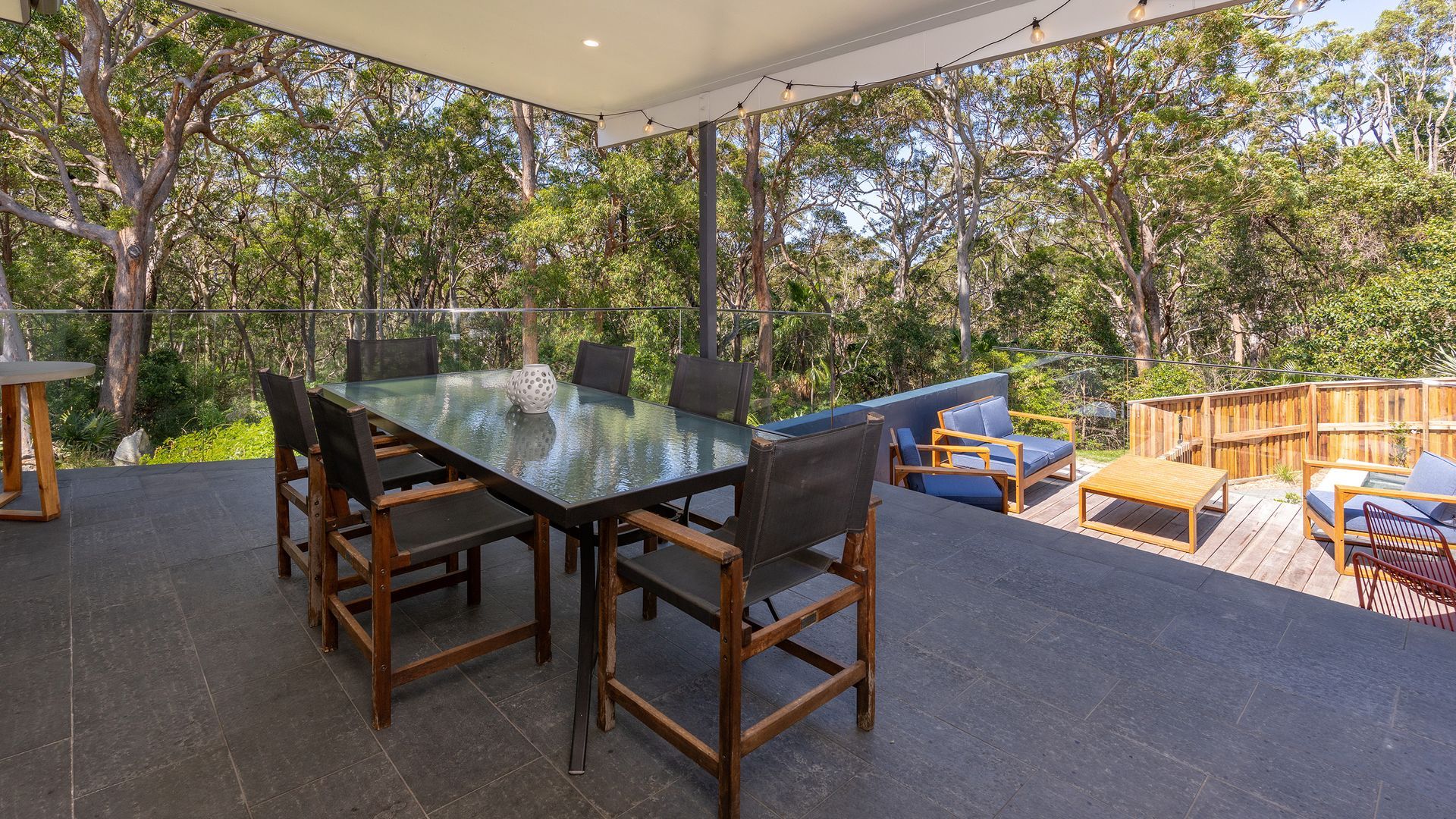 An outdoor patio with a glass-top table, wooden chairs, and a blue sofa.