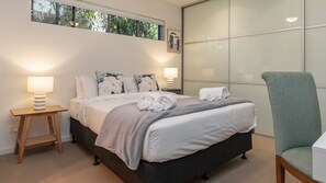 A neatly made bed with pillows and a blanket, a bedside lamp, and a chair.