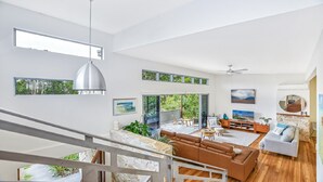 Amplia sala de estar con techo alto, ventanas grandes y una escalera que conduce a un nivel superior.