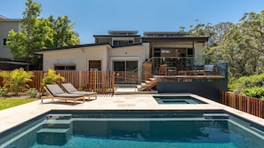 A modern house with a swimming pool, outdoor furniture, and a wooden fence.