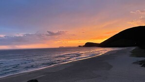 Una playa con un atardecer, olas y una montaña a lo lejos.