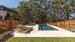 A backyard with a swimming pool, lounge chairs, and a wooden deck.