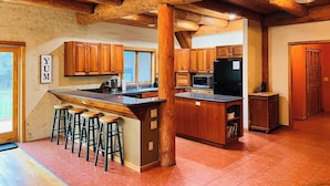 Une cuisine spacieuse avec des meubles en bois, un grand îlot central doté de tabourets et un panneau indiquant clairement « MIAM ».
