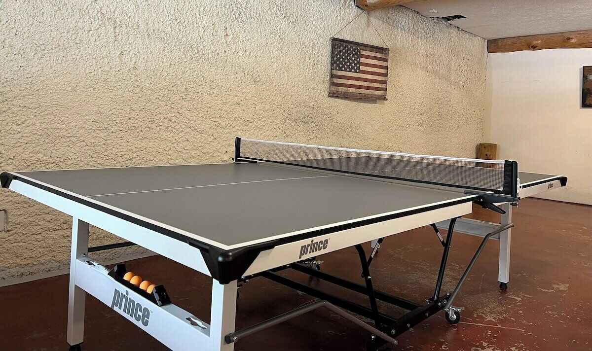 A table tennis table with a net, branded with 'prince', in a room with a textured wall and an American flag decoration.