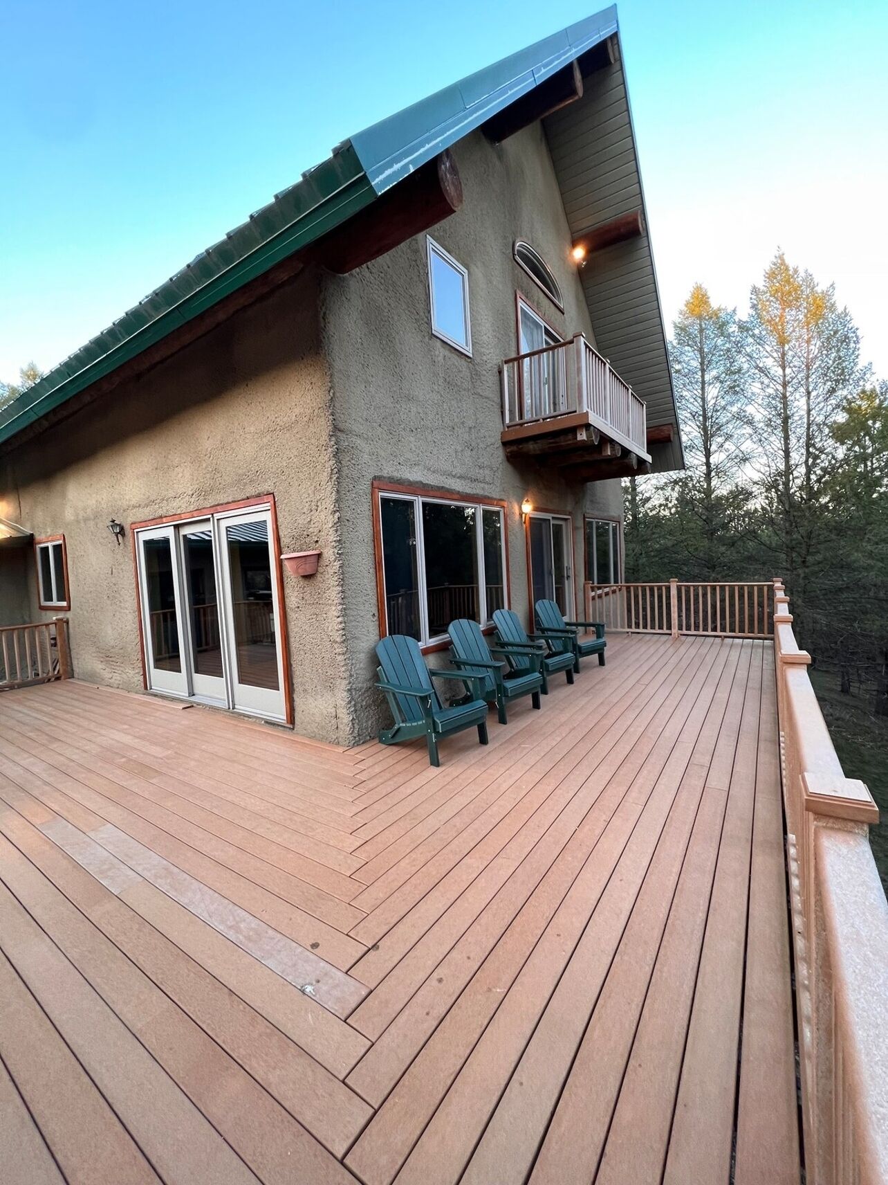 Ein zweistöckiges Gebäude mit einer Holzterrasse, Sitzgelegenheiten im Freien und einem Balkon.