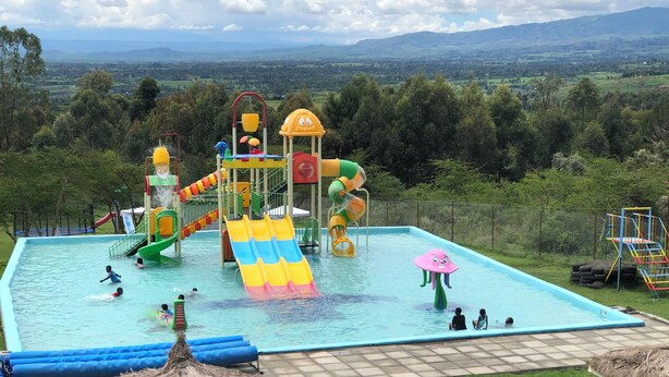 Parque acuático con toboganes y piscina, rodeado de vegetación y colinas.