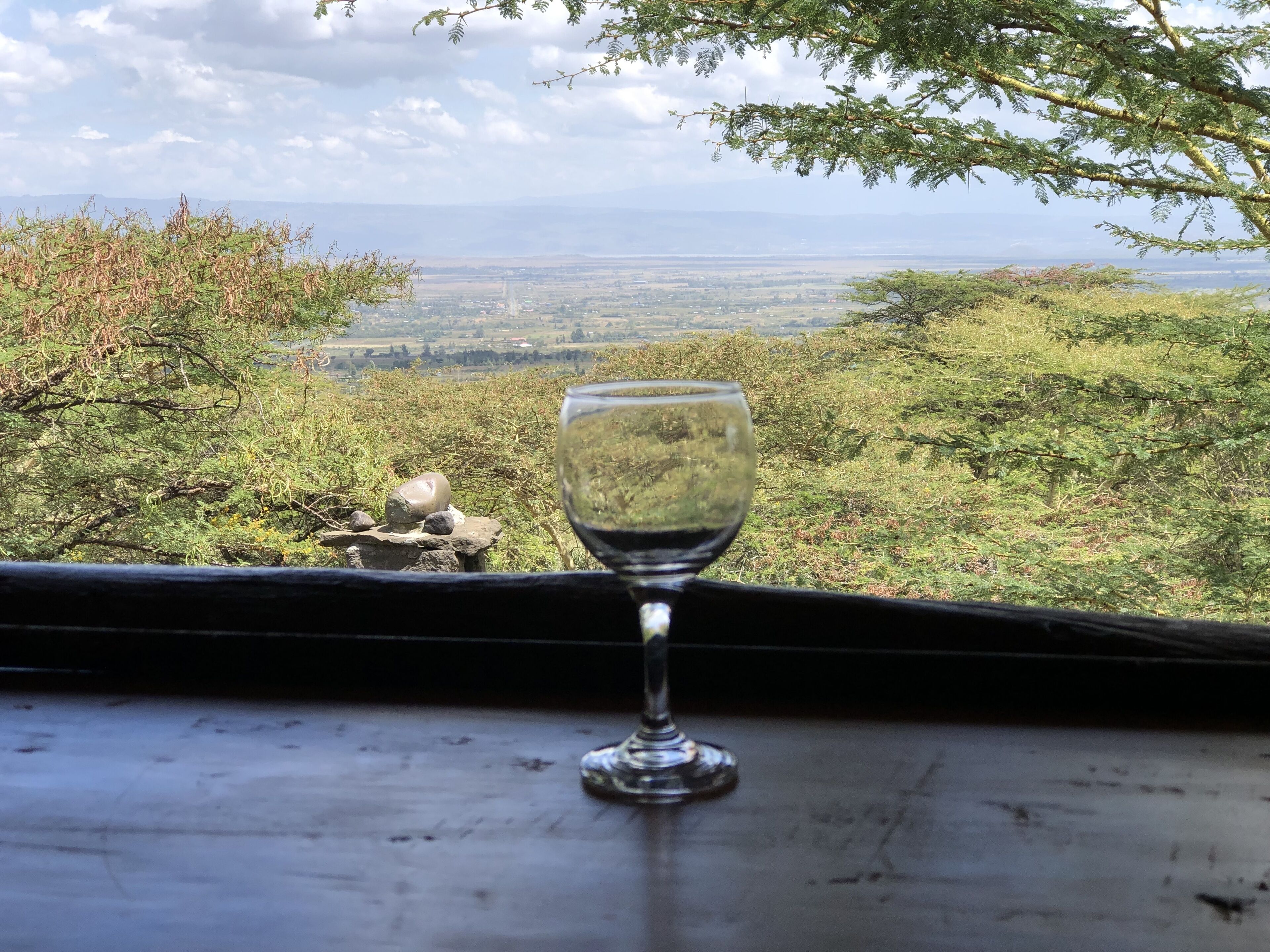 A glass of wine on a table with a view of a landscape.