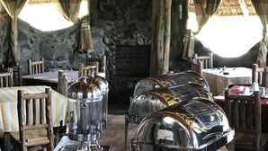 Un comedor rústico con mesas de madera, estaciones de servicio metálicas y una chimenea de piedra.